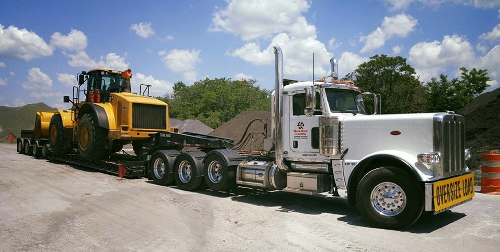 white oversize load truck hauling heavy construction equipment